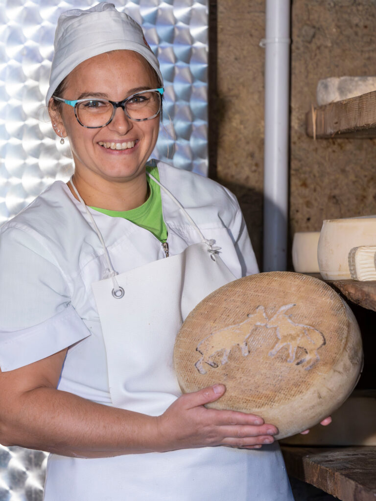 Agricuore Elisa bozzorolando con un formaggio nella cella di stagionatura